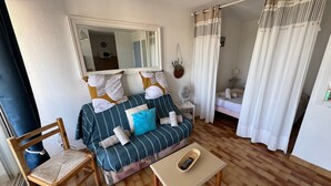 Et hyggeligt rum med sofa, stol, lille bord, spejl og seng.