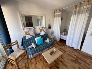 A cozy room with a sofa, a chair, a small table, a mirror, and a bed. - L’Escapade du Cap, Sea View, Sleeps 6 (Le Cap d'Agde)