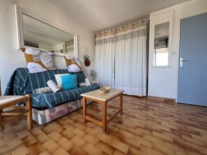 A room with a sofa, a small table, a mirror, a fan, and a door. - L’Escapade du Cap, Sea View, Sleeps 6 (Le Cap d'Agde)