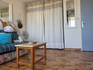 A room with a sofa, a small wooden table, a mirror, and a door. - L’Escapade du Cap, Sea View, Sleeps 6 (Le Cap d'Agde)