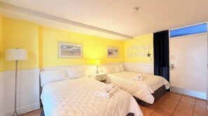 Ein Hotelzimmer mit zwei Betten, einem Nachttisch mit Lampe, einer Tür mit Sternenverzierung und einem Wandbild mit Strandmotiv.