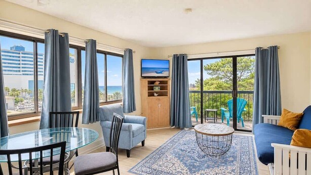 Ein Zimmer mit Glastisch, Stühlen, einer Couch, einem Fernseher und Meerblick.