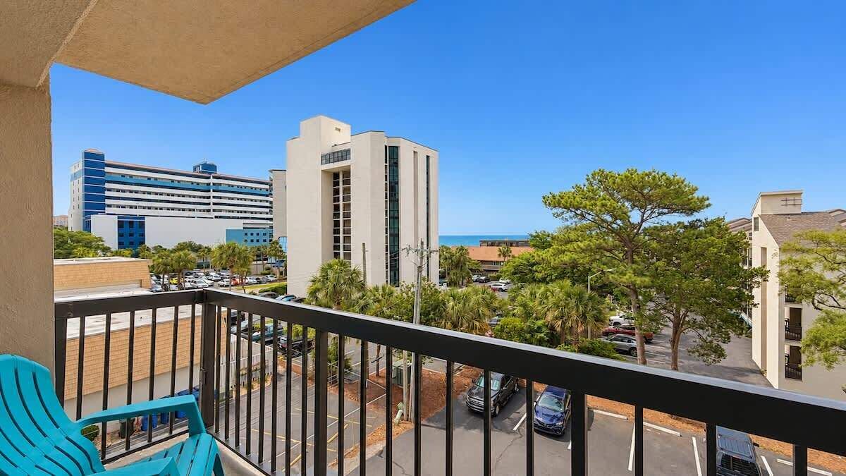A balcony with a view of a parking lot, buildings, and trees.