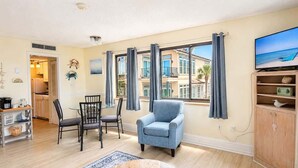 Ein Wohnzimmer mit Essbereich, einem blauen Sessel, einem Fernseher und Meerblick durch große Fenster.