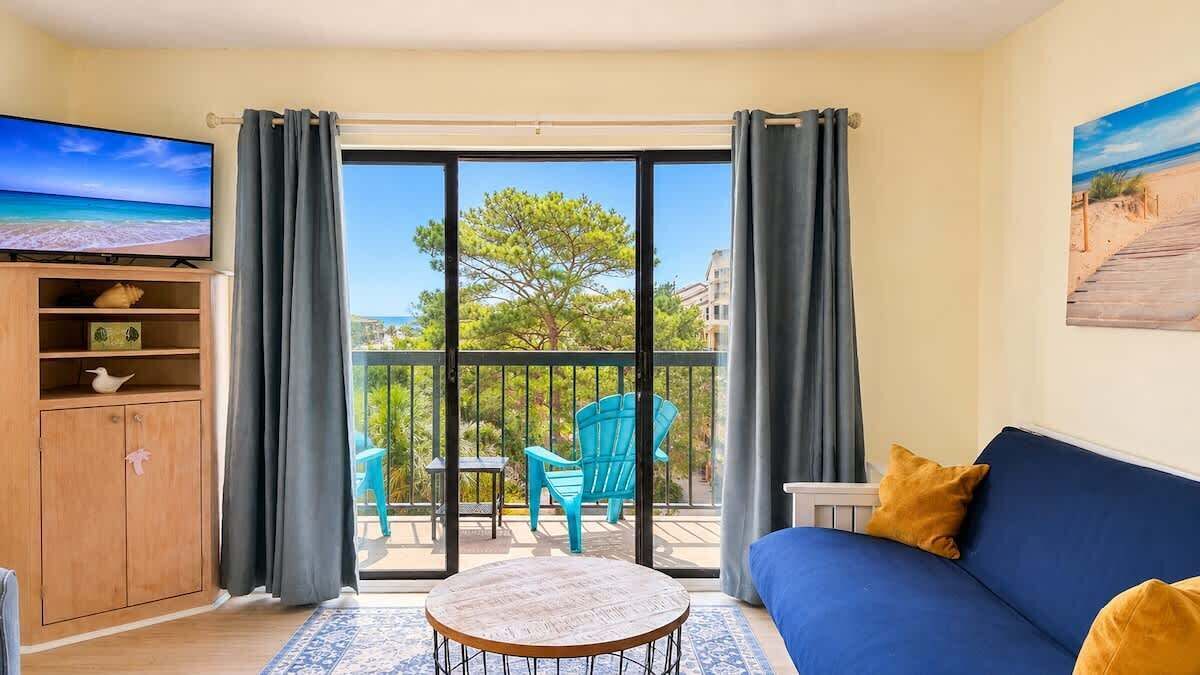 A living room with a sofa, a television, a wooden cabinet, and a balcony with chairs and a table.