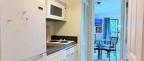 A compact kitchen with white cabinets, a microwave, and a stove. There is a dining area with a table and chairs visible through an open door.