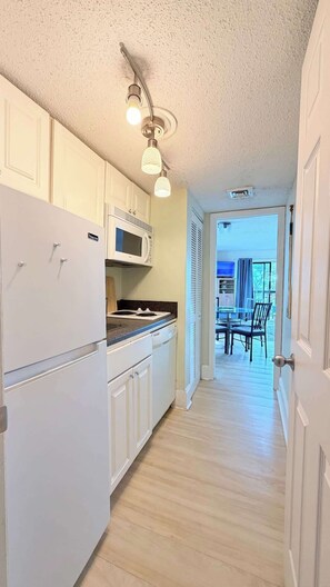 A compact kitchen with white cabinets, a microwave, and a stove. There is a dining area with a table and chairs visible through an open door. - Beachside Condo Near Ocean | Pool | Sleeps 6 (Myrtle Beach)