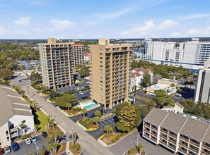 A high-rise building with multiple floors, surrounded by parking areas and greenery. - Beachside Condo Near Ocean | Pool | Sleeps 6 (Myrtle Beach)