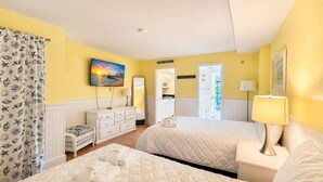 Ein Hotelzimmer mit zwei Betten, einem Fernseher, einem Gemälde, einem Schreibtisch mit Lampe und einem durch eine offene Tür einsehbarer Badezimmer.