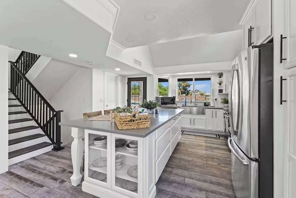 A modern kitchen with white cabinetry, a central island, and a stainless steel refrigerator. - Themed Luxury Retreat | Pool, BBQ & Arcade (Gilbert)