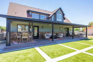 A house with a covered patio, stone accents, and a well-maintained lawn. - Themed Luxury Retreat | Pool, BBQ & Arcade (Gilbert)