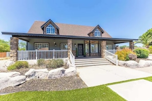 A two-story house with a stone facade, a covered porch, and a landscaped front yard. - Themed Luxury Retreat | Pool, BBQ & Arcade (Gilbert)