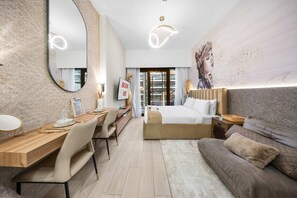 A modern hotel room with a large bed, a desk with a chair, a sofa, a large mirror, and a wall with a floral mural. - Free Housekeeping Visits During Your Stay - Stayshort - Cozy Studio in Meydan for 2 Close to Golf Courses (Dubai)