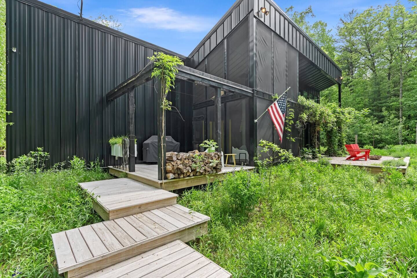 Une terrasse extérieure moderne, équipée d’un barbecue, d’un fauteuil Adirondack rouge et d’un drapeau américain.