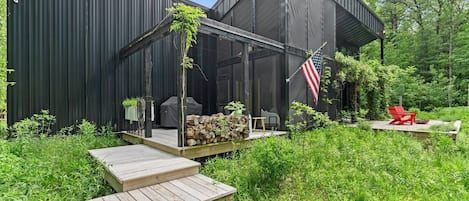 Une terrasse extérieure moderne, équipée d’un barbecue, d’un fauteuil Adirondack rouge et d’un drapeau américain.