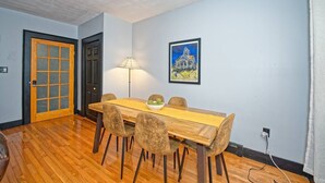 A dining area with a wooden table, four chairs, a lamp, and a framed picture on the wall.
