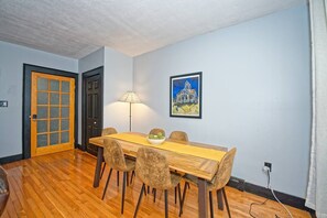 Ein Essbereich mit einem Holztisch, vier Stühlen, einer Lampe und einem gerahmten Bild an der Wand.