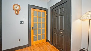 A hallway with a wooden door, a wall clock, and a floor lamp.