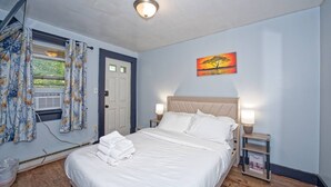 A bedroom with a bed, a nightstand, a lamp, a painting, and a window with curtains.