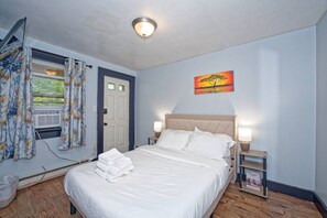 Ein Schlafzimmer mit einem Bett, einem Nachttisch, einer Lampe, einem Gemälde und einem Fenster mit Vorhängen.