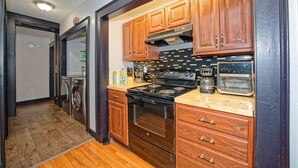 A compact kitchen with wooden cabinets, a stove, a microwave, and a coffee maker.