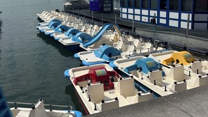 A marina with several small boats docked, a building labeled 'Hersa Events,' and a clear sky.