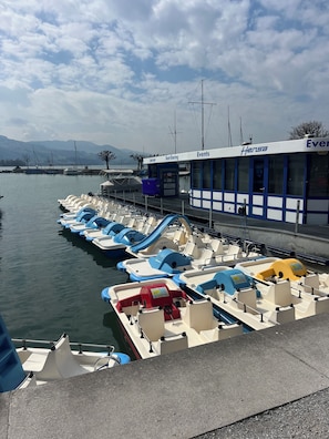Un port de plaisance où sont amarrés plusieurs petits bateaux, un bâtiment portant l’inscription « Hersa Events », et un ciel dégagé.