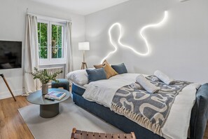 Quarto moderno com cama, mesa de cabeceira, abajur e uma instalação luminosa única na parede.