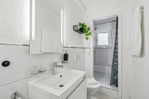 Casa de banho moderna com lavatório branco, espelho e zona de duche.