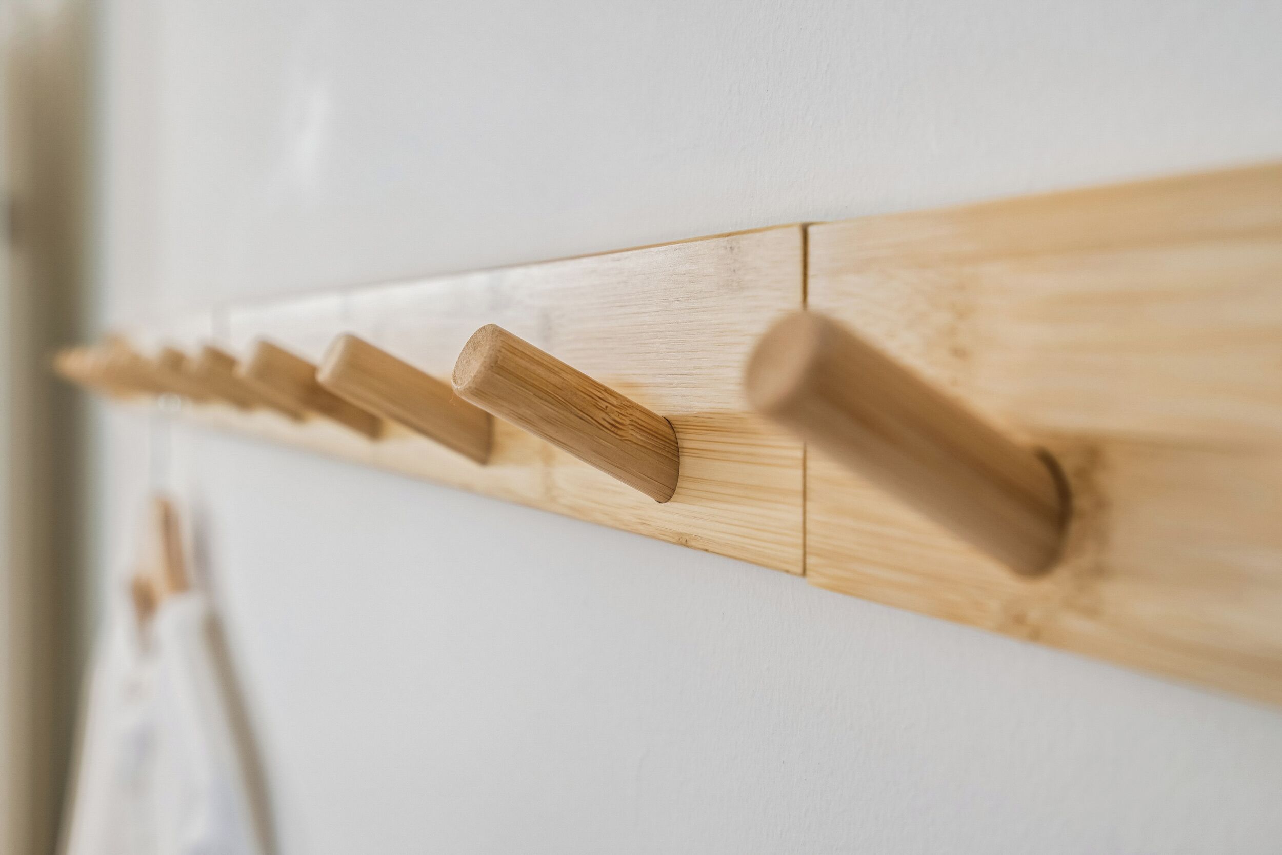 A wooden coat rack with multiple hooks against a white wall.