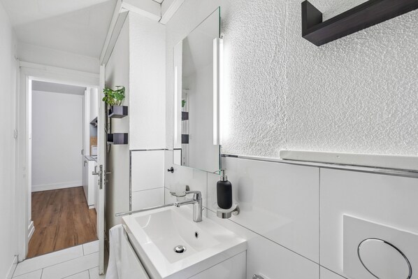 Een moderne badkamer met een wit wastafelmeubel, spiegel en een glazen plankje met een plant.