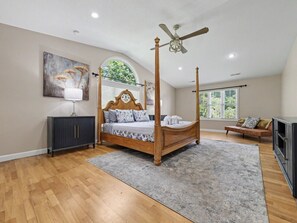 Ein Schlafzimmer mit einem Himmelbett, einer dunklen Kommode, einer Couch und einem großen Fenster.