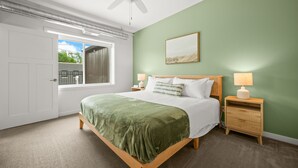 Un dormitorio con cama, mesitas de noche, ventilador de techo, ventana con persianas y una pared verde.