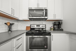 A kitchen with white cabinets, a stainless steel stove, a microwave, and a coffee maker.