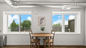 Un comedor con una mesa y sillas de madera, una planta en maceta y un cuadro en la pared.