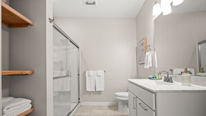 Un baño moderno con cabina de ducha de vidrio, inodoro, lavamanos con espejo y un perchero para toallas.