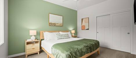Un dormitorio con una cama, una mesita de noche, una lámpara, un ventilador de techo y una puerta.