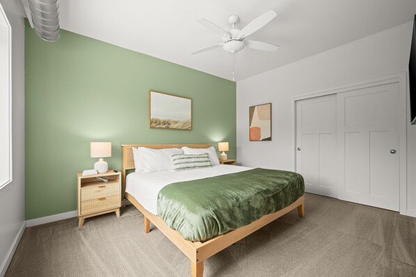 A bedroom with a bed, a nightstand, a lamp, a ceiling fan, and a door.