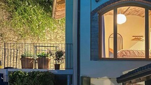 Ein zweistöckiges Haus mit Balkon, Blumentöpfen und einem sichtbaren Innenraum mit Möbeln.