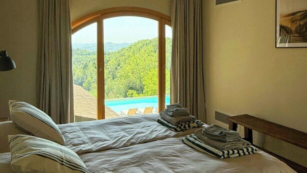 Ein Schlafzimmer mit einem großen Bett, Blick auf eine Berglandschaft und einer Holzbalkendecke.