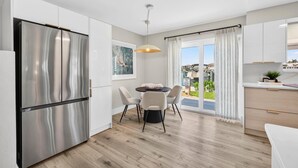 A modern kitchen with a stainless steel refrigerator, a dining table with chairs, and a view of the outside through large windows. - Bayfront Waterview Newly Upgraded Condo Clearwater Beach (Clearwater)