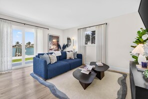 Un salon moderne avec un canapé bleu, une table basse et une vue sur une étendue d’eau, visible à travers de grandes fenêtres.