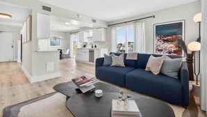 A modern living room with a blue sofa, a coffee table, and a kitchen in the background. - Bayfront Waterview Newly Upgraded Condo Clearwater Beach (Clearwater)