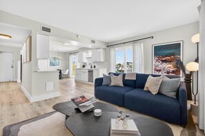 Ein modernes Wohnzimmer mit einem blauen Sofa, einem Couchtisch und einer Küche im Hintergrund.