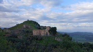 Ein historisches Gebäude mit Ruinen auf einem Hügel, umgeben von Grün und mit weiter Aussicht aufs Meer.