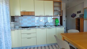Eine Küche mit hellen Schränken, einem grünen Gerät und einem Essbereich mit Holztisch und -stühlen.