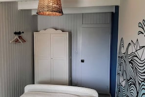 A bedroom with a bed, a wardrobe, a hanging light fixture, and a wall with a graphic design. - Cosy house & private garden - Beaches 5 min away (Tourville-sur-Sienne)