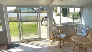 Una veranda riparata con porte scorrevoli in vetro, mobili in vimini e vista su un'area verde.