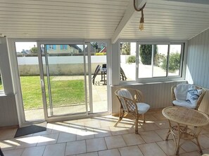 A covered patio with sliding glass doors, wicker furniture, and a view of a grassy area. - Cosy house & private garden - Beaches 5 min away (Tourville-sur-Sienne)