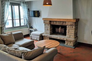 A living room with a stone fireplace, a sofa, a coffee table, and a television. - Cosy house & private garden - Beaches 5 min away (Tourville-sur-Sienne)